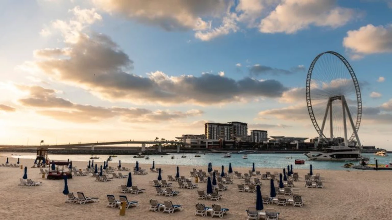Sun loungers and blue umbrellas lined up on the sand at JBR Beach with Ain Dubai across the water