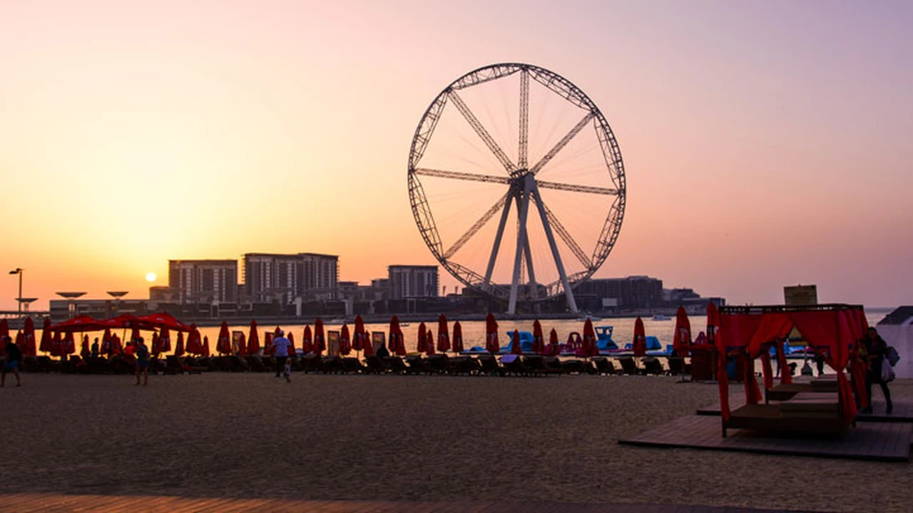 Ain Dubai observation wheel glowing at sunset seen from JBR Beach with red beach umbrellas in the foreground