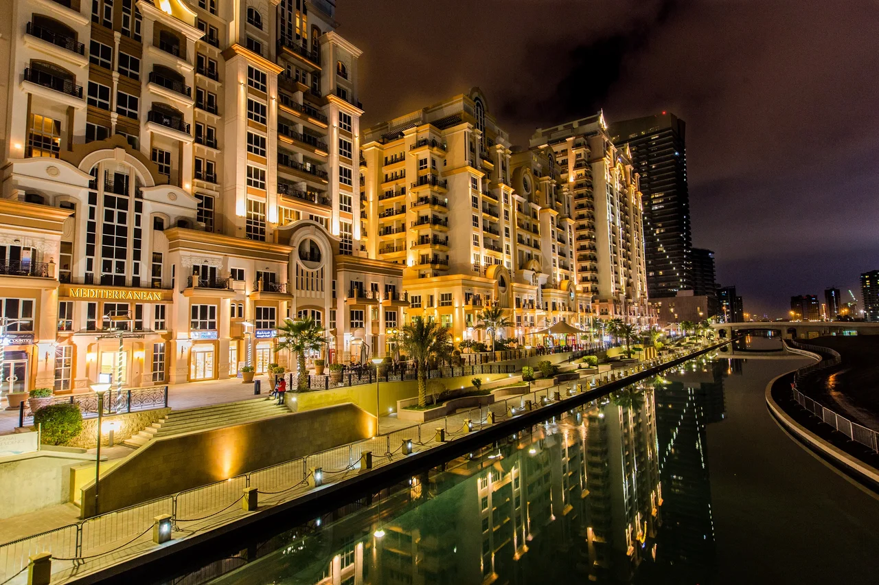 Canal Residence West towers along the canal promenade in Dubai Sports City at night